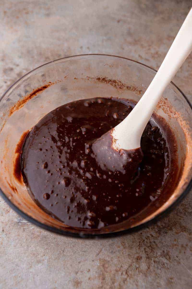 Glossy chocolate brownie batter in a glass bowl with a white spatula.