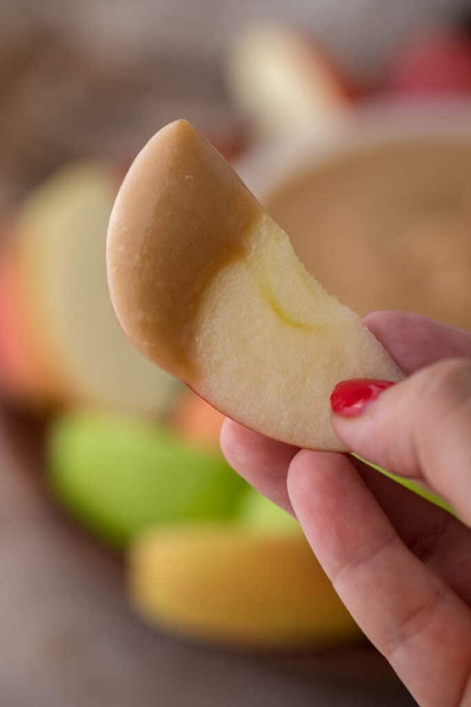 Hand holding apple slice dipped in caramel