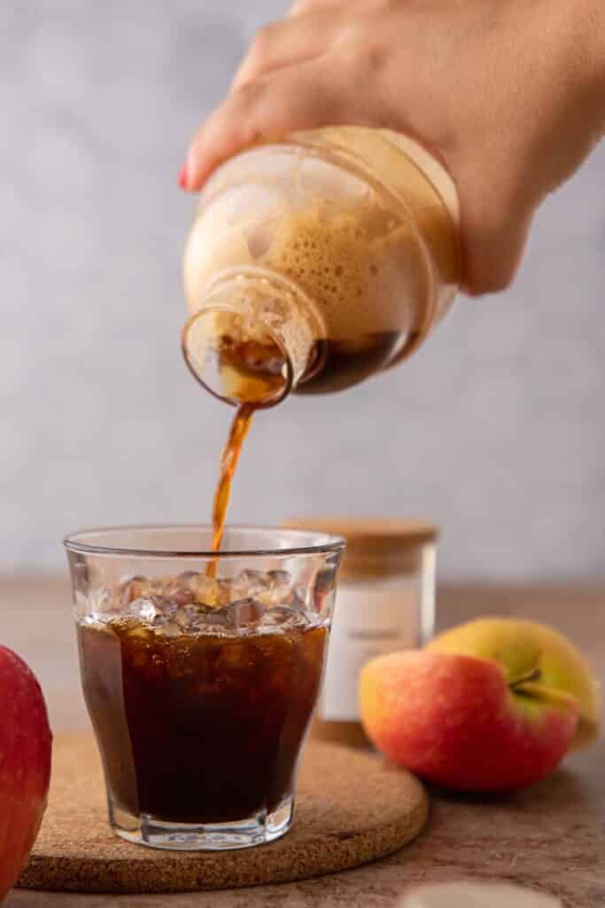 Pouring homemade Starbucks apple crisp oatmilk shaken espresso from a cocktail shaker over ice with fresh apples