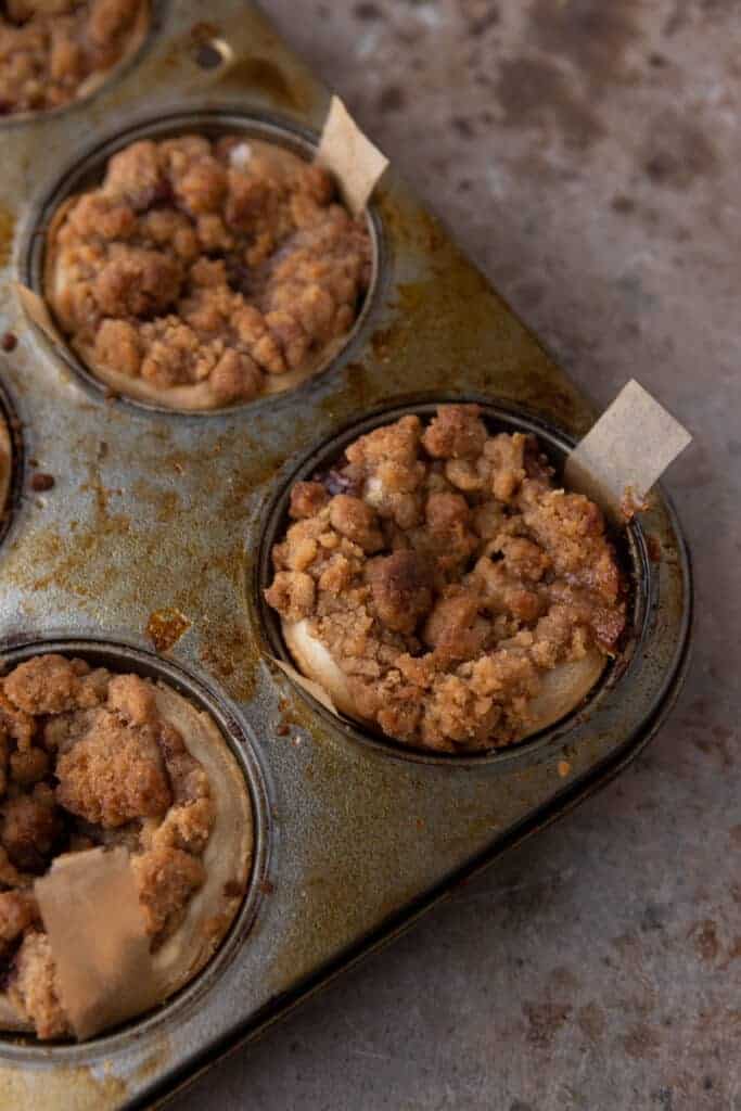 Baked mini apple pies in a muffin tin showing thin strips of parchment paper to pull them out.