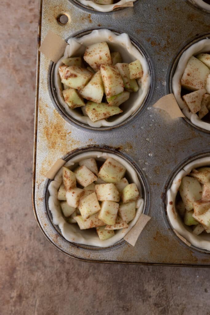 unbaked apple sitting in pie shells in a muffin tin