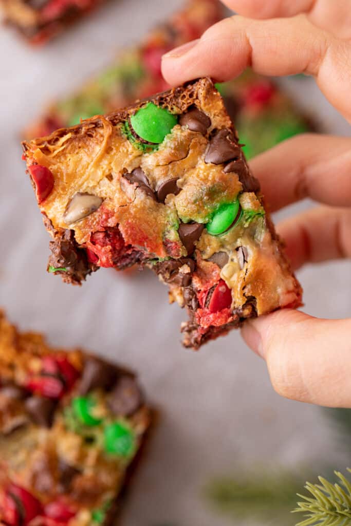 a christmas magic cookie bar with a bite taken out being held up by a hand
