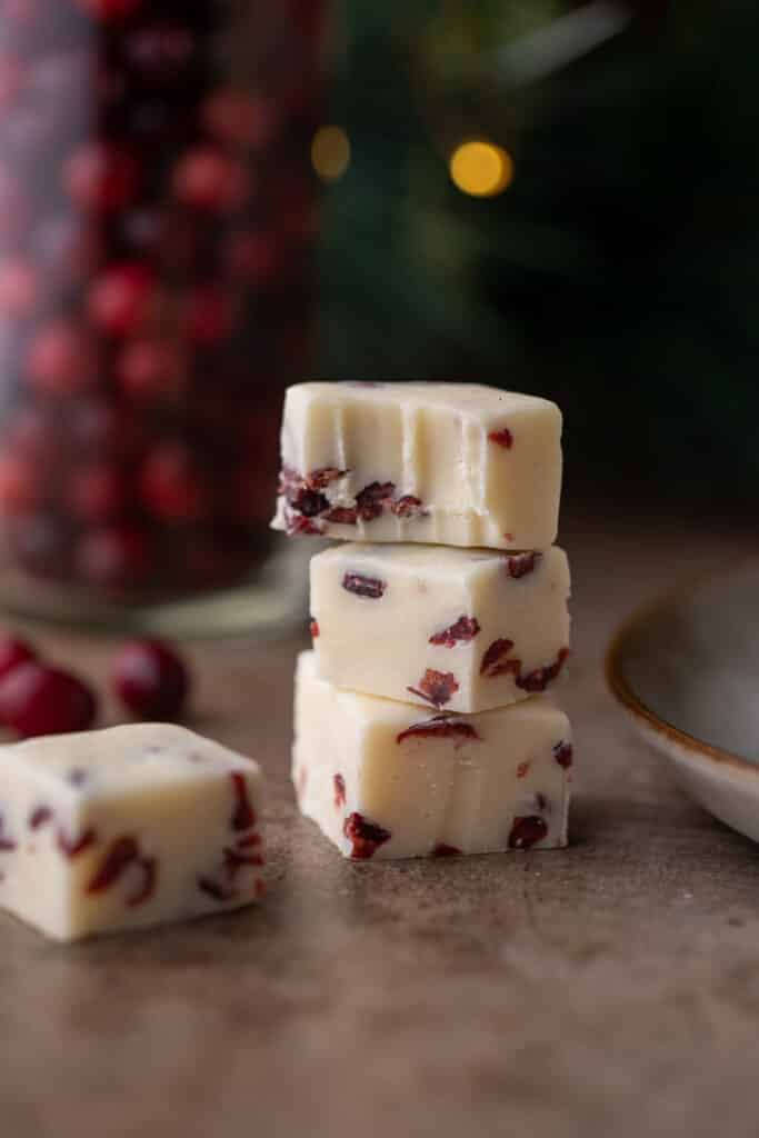 three cranberry white chocolate fudge squares stacked on top of each other with a bite taken out of the top one