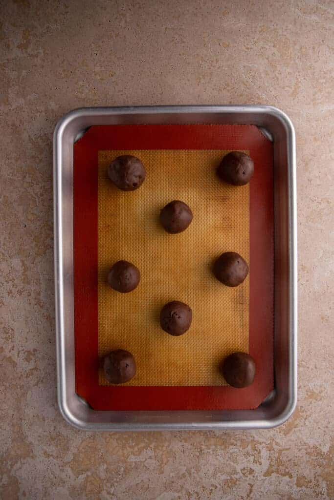 Chocolate cookie dough rolled into balls on a lined baking sheet.
