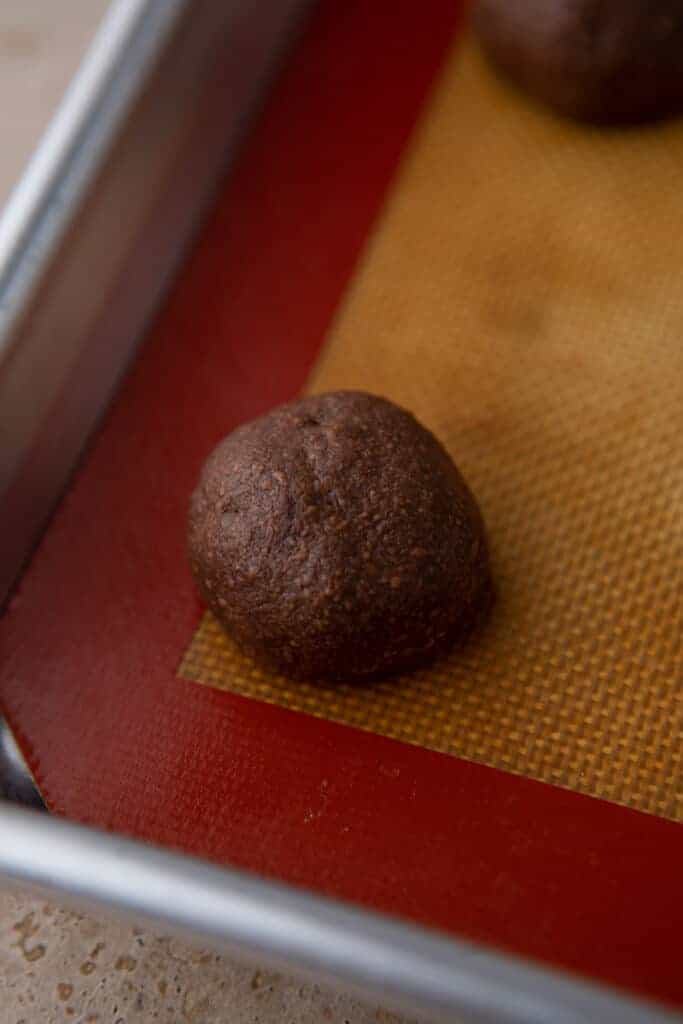 Close-up of a chocolate cookie dough ball on a silicone baking mat.