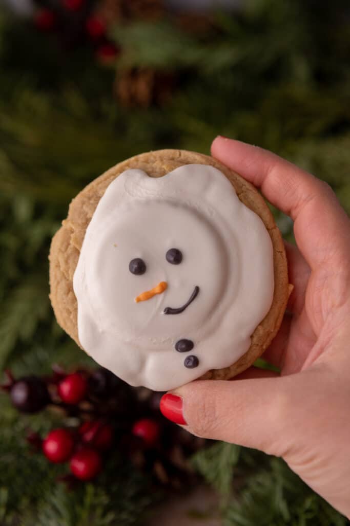 a hand holding up a single melted snowman peanut butter cookie