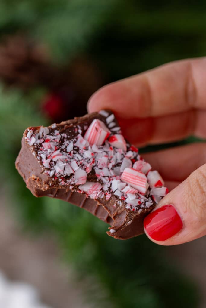 a square of peppermint fudge with a bite taken out of it being held up by a hand
