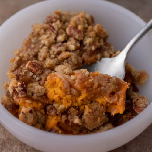 spoon in a bowl full of sweet potato casserole with pecan topping