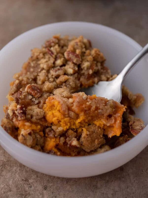 spoon in a bowl full of sweet potato casserole with pecan topping