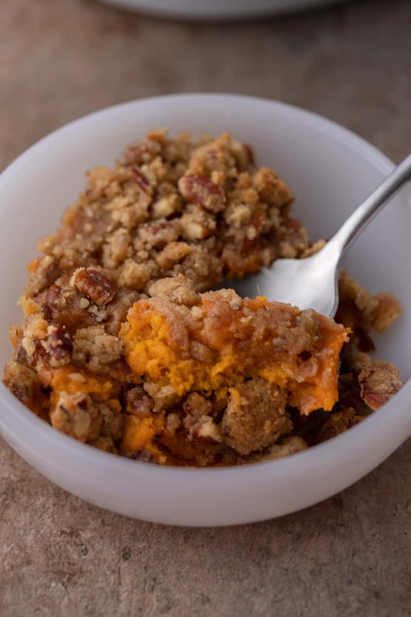 spoon in a bowl full of sweet potato casserole with pecan topping