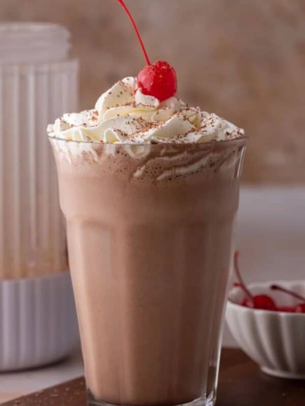 Homemade chocolate milkshake in a tall glass with a topping of whipped cream swirl and a cherry.