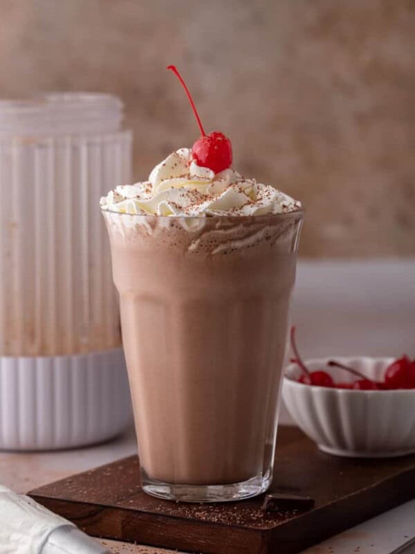 side view of the chocolate milkshake recipe with a blender behind it