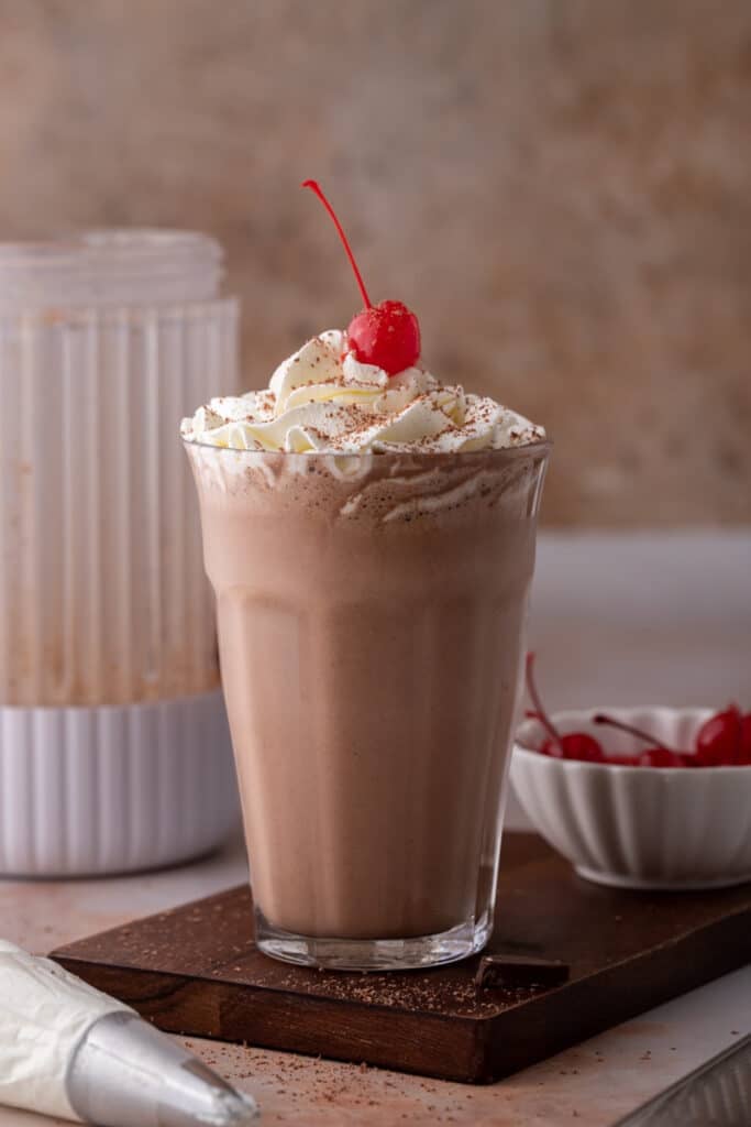 side view of the chocolate milkshake recipe with a blender behind it