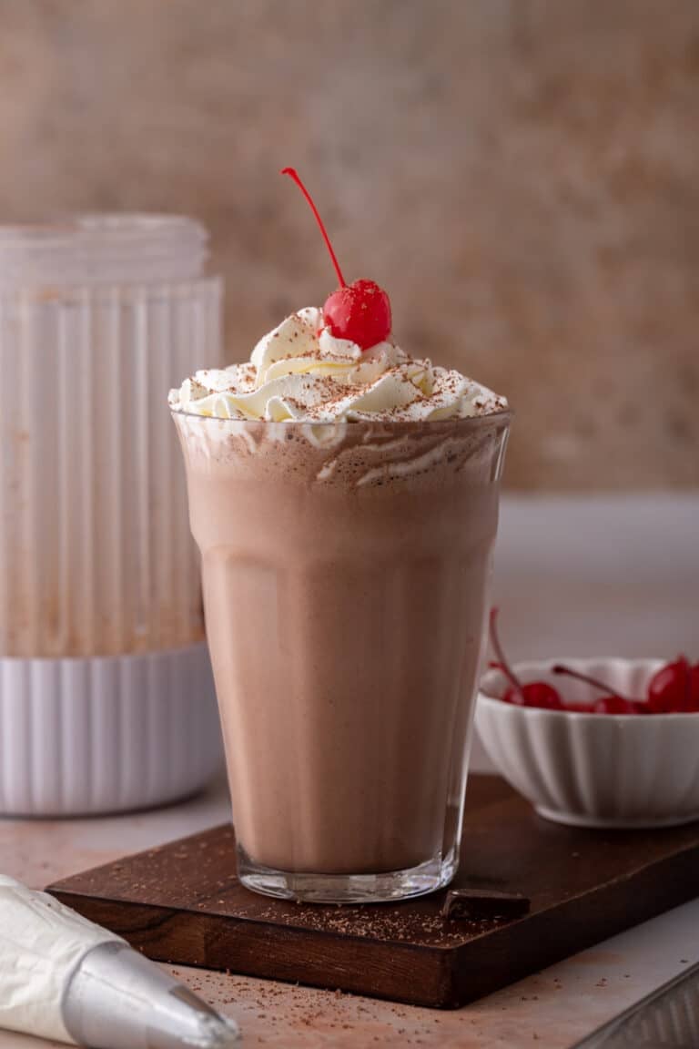 side view of the chocolate milkshake recipe with a blender behind it