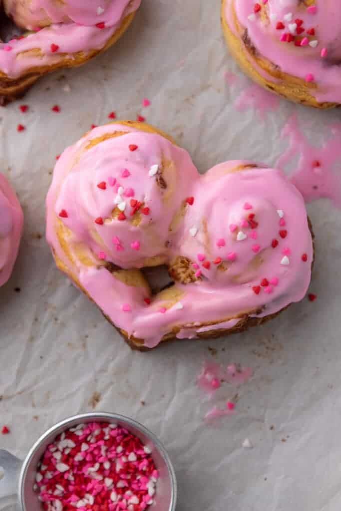 Heart shaped cinnamon rolls with pink frosting and Valentine sprinkles