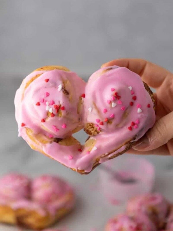 a valentine's day heart shaped cinnamon roll being held up by a hand