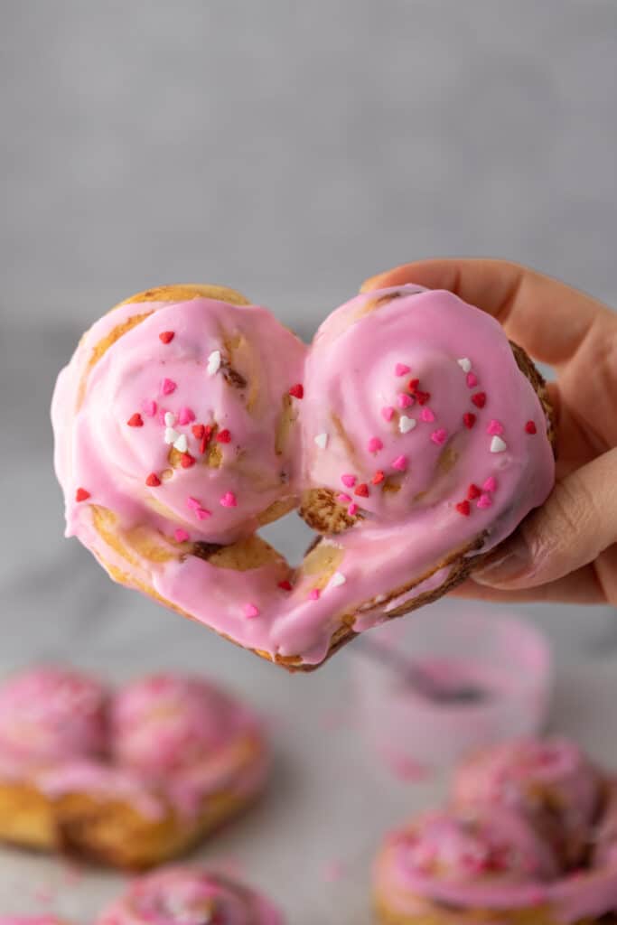 a valentine's day heart shaped cinnamon roll being held up by a hand