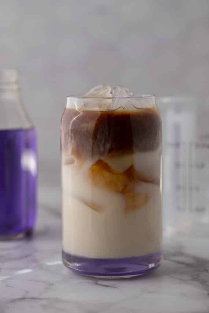 Homemade Starbucks iced lavender oatmilk latte with espresso swirling into milk with a purple lavender syrup bottle