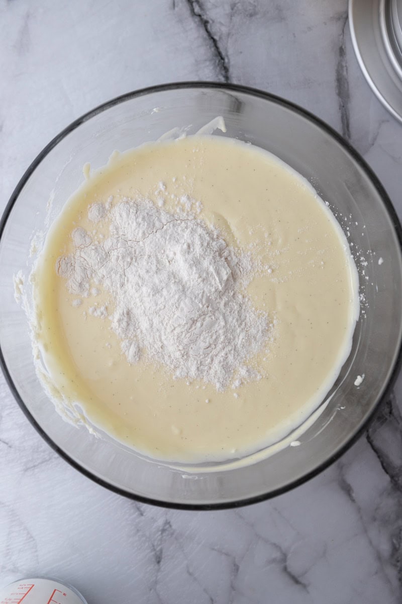 Flour and cornstarch added on top of the cheesecake batter in a glass bowl.