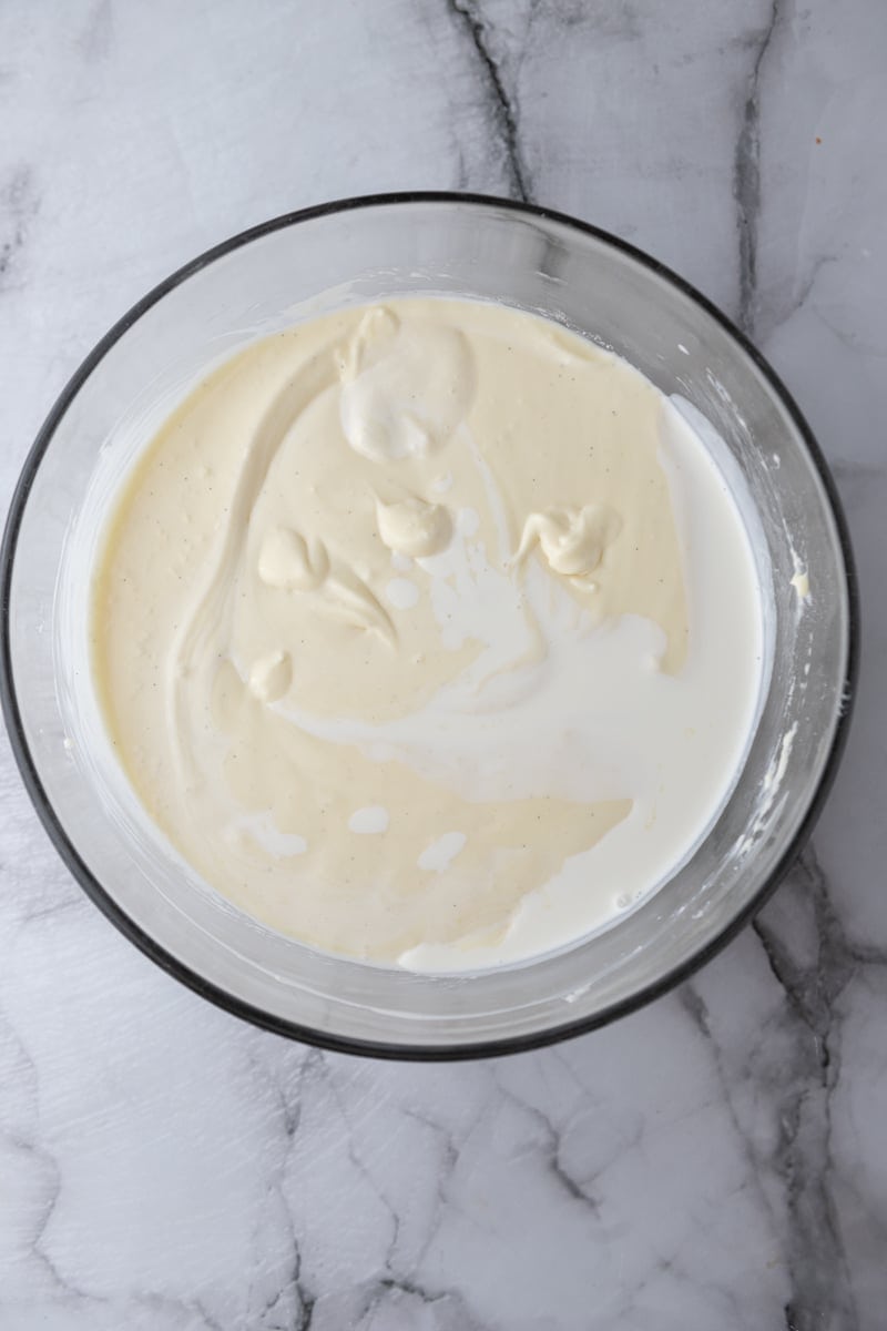 Heavy cream being mixed into the cheesecake batter in a glass bowl.