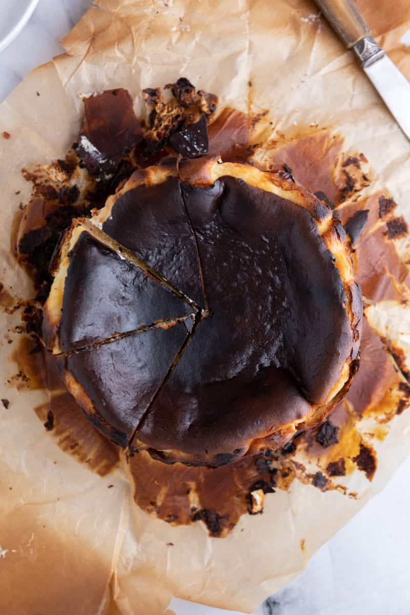 Overhead view of a sliced 6-inch burnt Basque cheesecake on parchment paper.