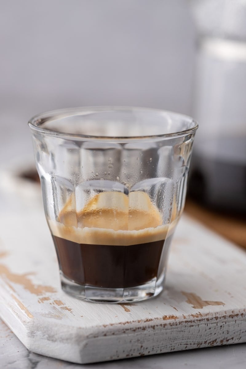 A freshly pulled shot of espresso with a layer of crema in a small clear glass.