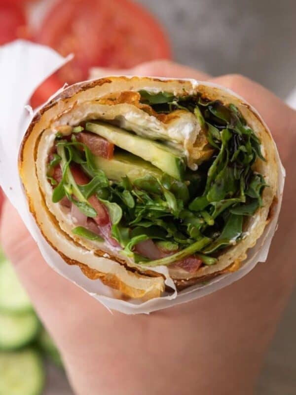 Hand holding a rolled egg white wrap stuffed with greens and sliced vegetables.