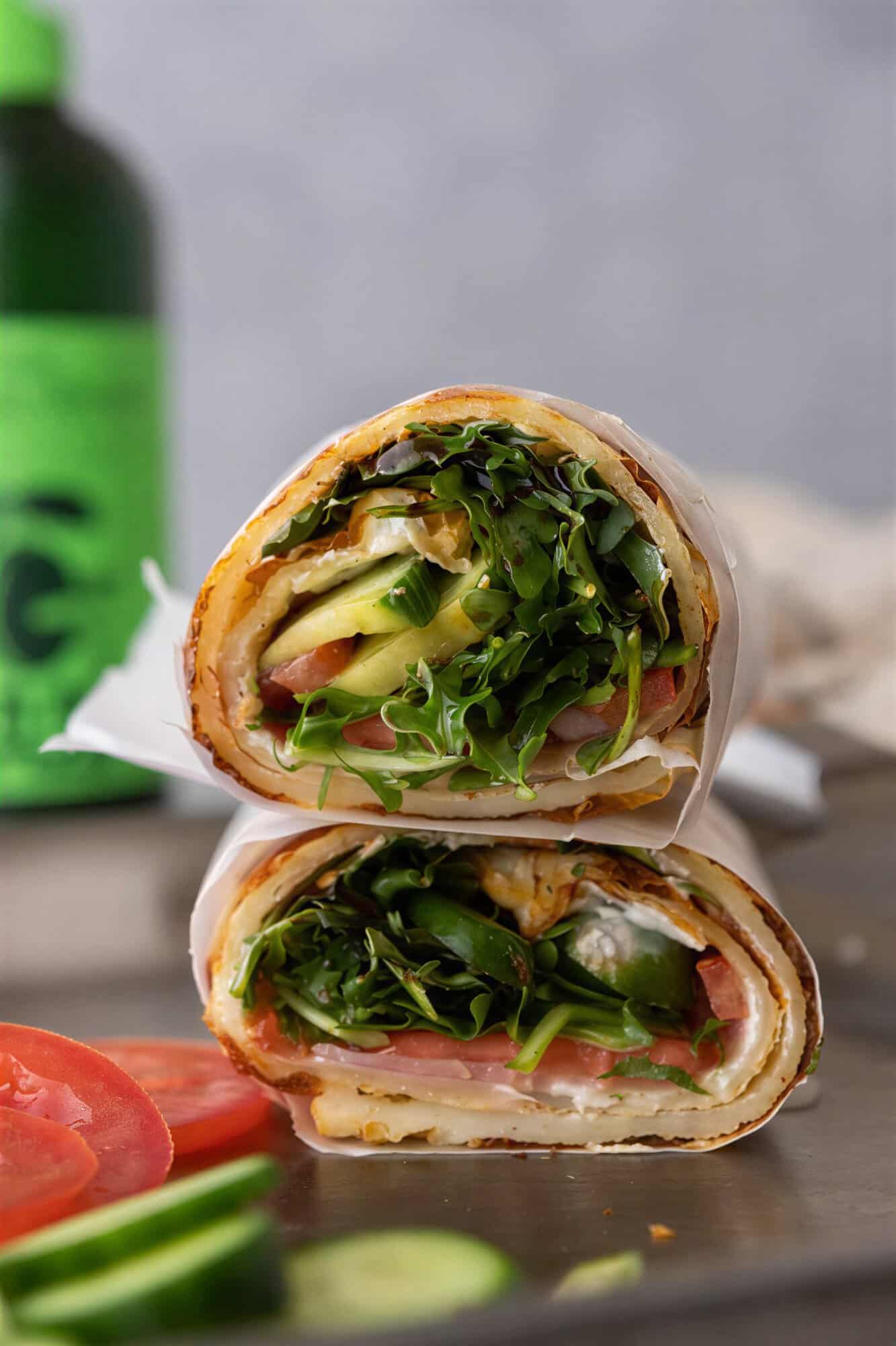 High protein egg white wrap cut in half and filled with arugula, avocado, tomato, and cucumber.