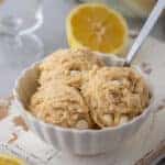A white bowl of edible lemon cookie dough scoops with white chocolate chips and a spoon.