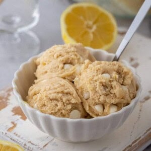 A white bowl of edible lemon cookie dough scoops with white chocolate chips and a spoon.