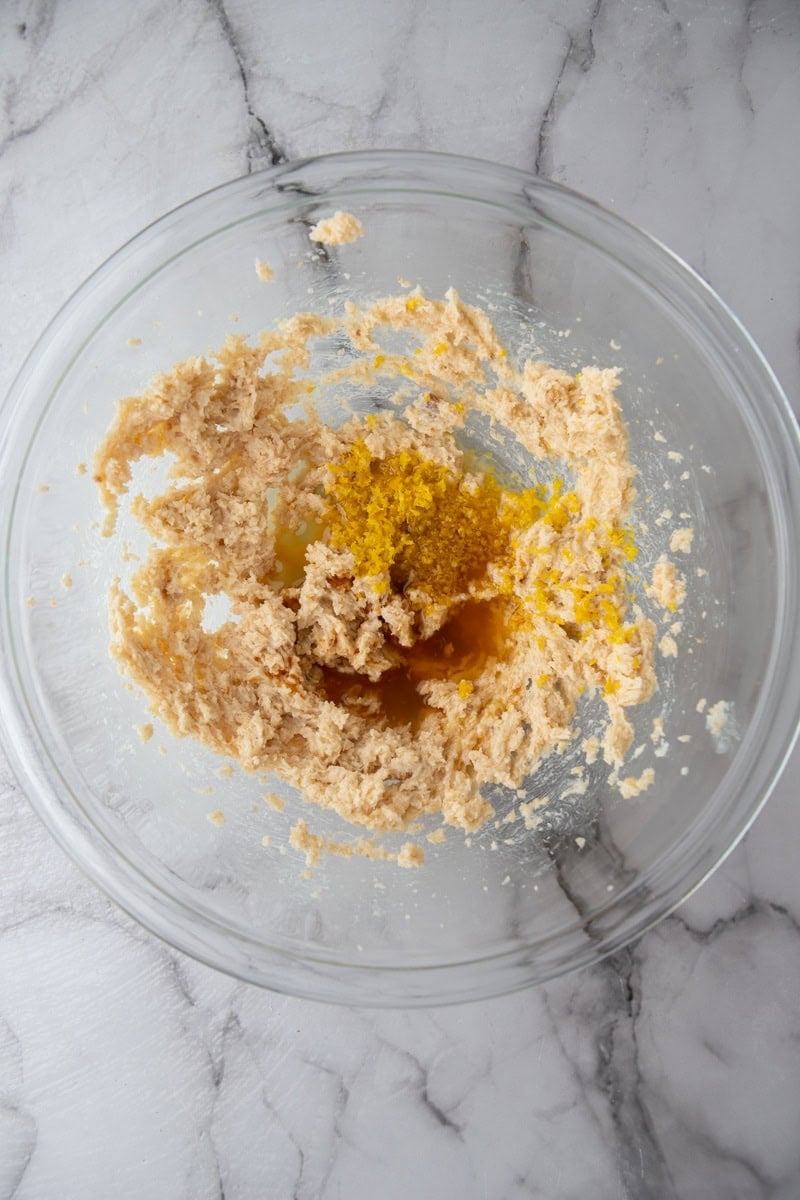 Creamed butter and sugar topped with lemon zest, lemon juice and vanilla in a glass bowl.