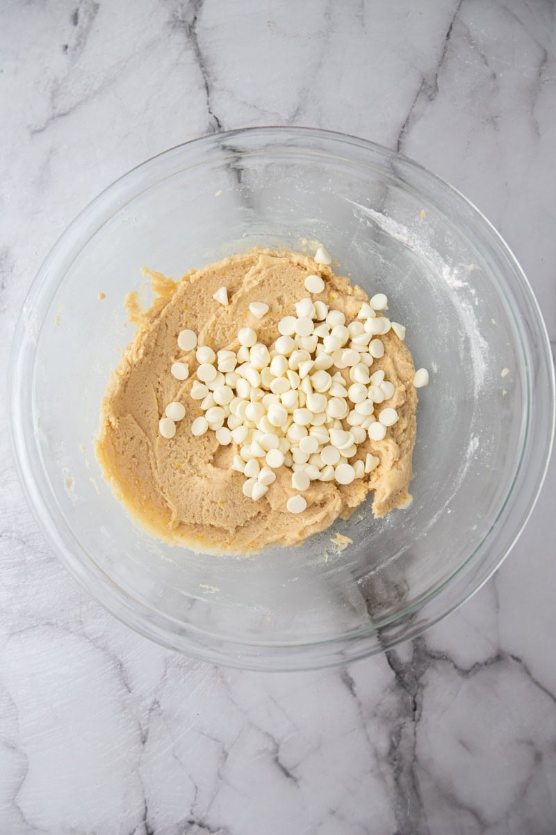 White chocolate chips on top of lemon cookie dough in a glass bowl.
