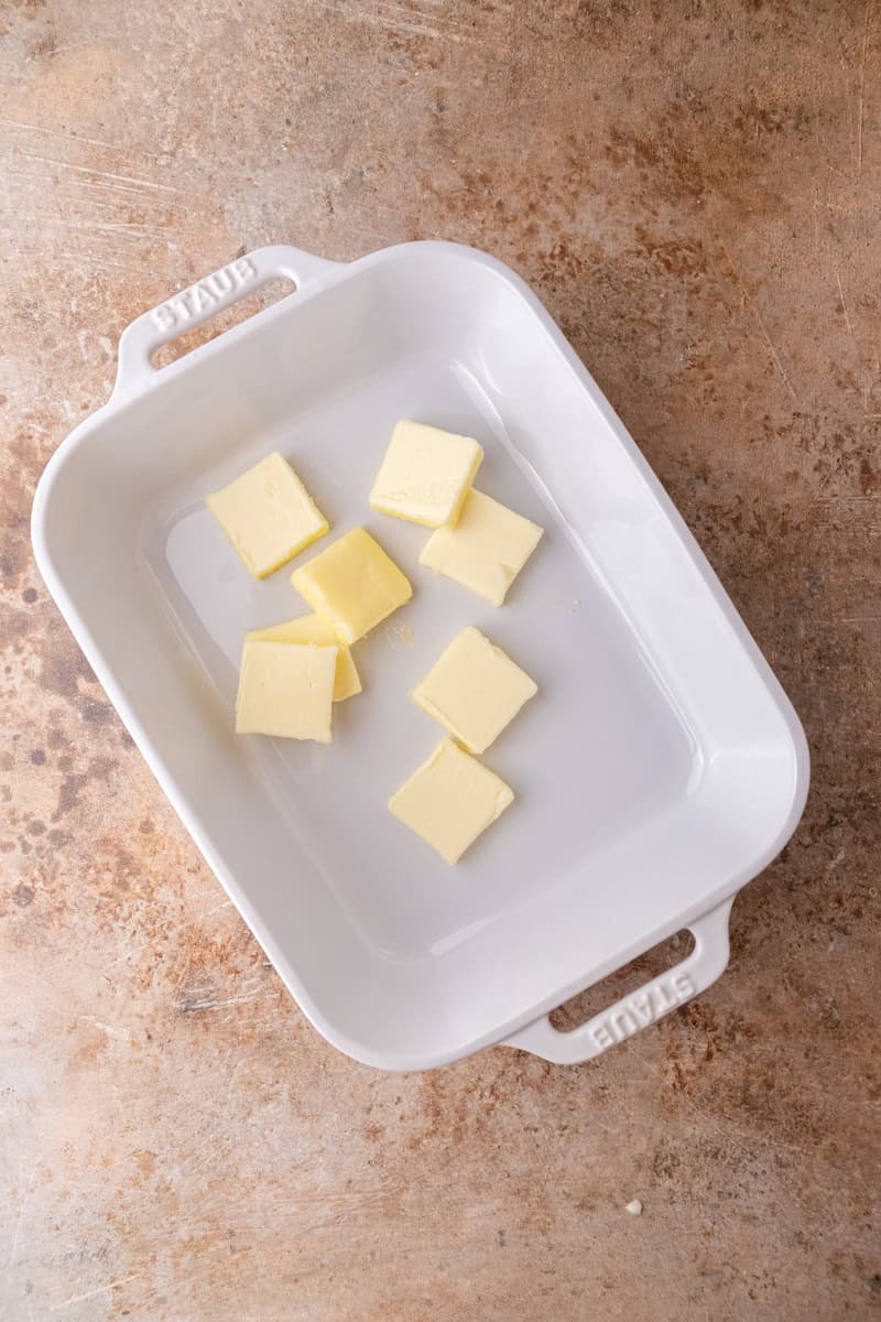 Cubed butter in a 9x13 baking dish ready to melt in the oven.