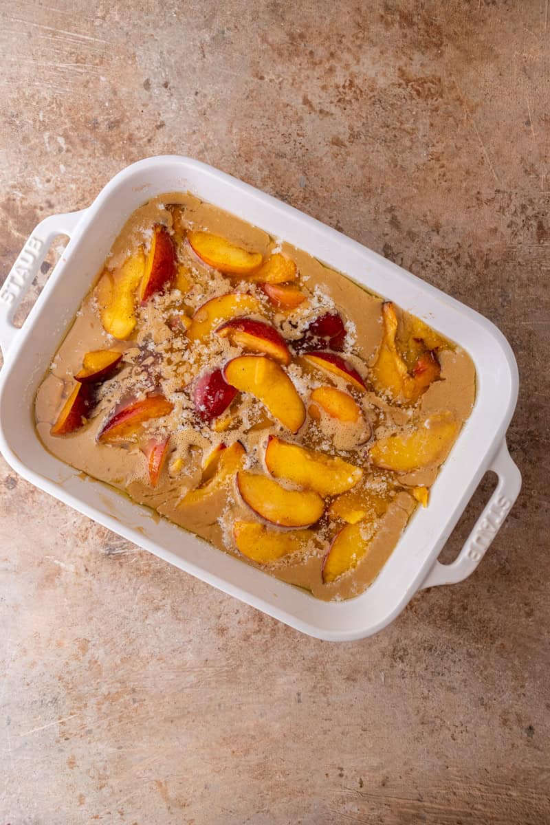 Peaches spooned over the cobbler batter in a baking dish.