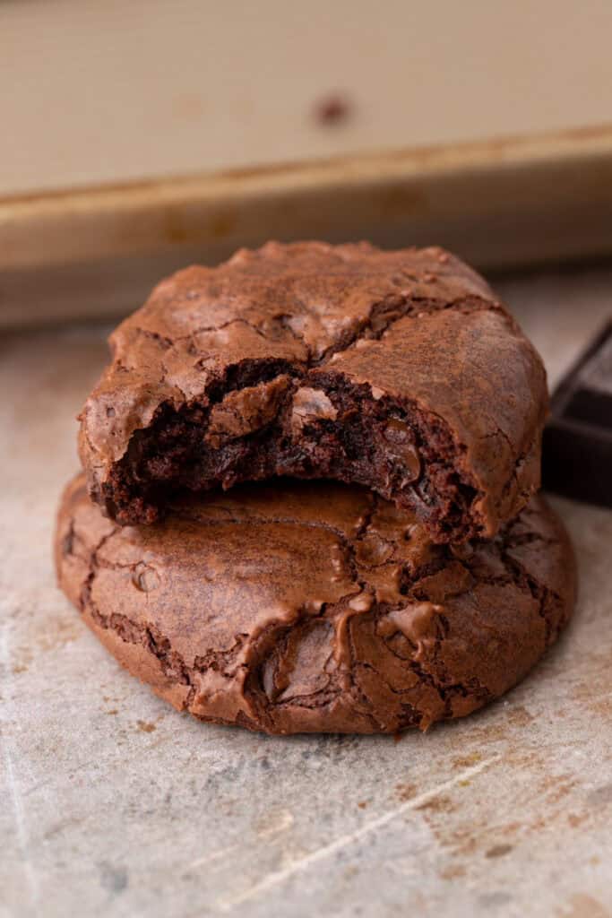 Two small batch brownie cookies stacked with the top cookie broken in half to show the fudgy melted chocolate interior next to dark chocolate squares