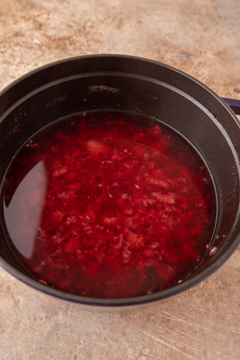 Raspberries simmered down into a deep red syrup in a dark pot.
