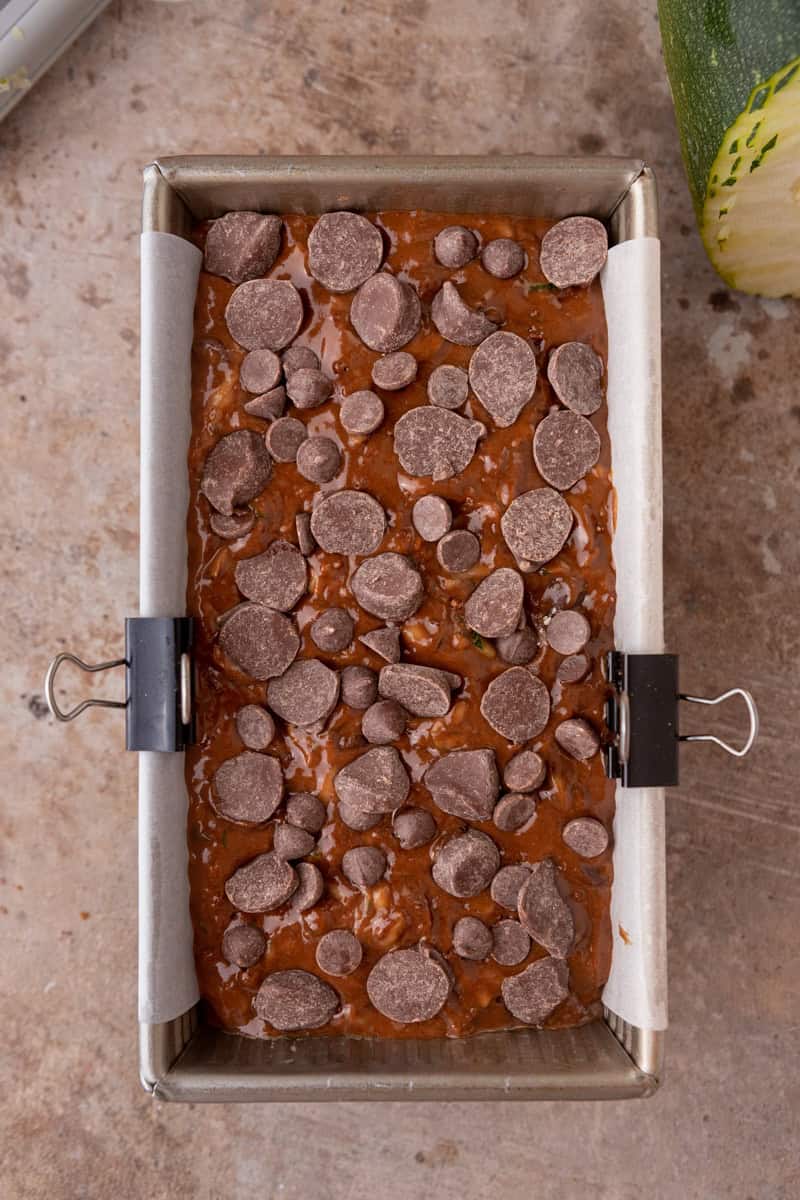 Chocolate zucchini bread batter in a parchment-lined loaf pan topped with dark chocolate chunks.