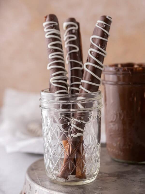 three caramel chocolate covered pretzel rods in a cup