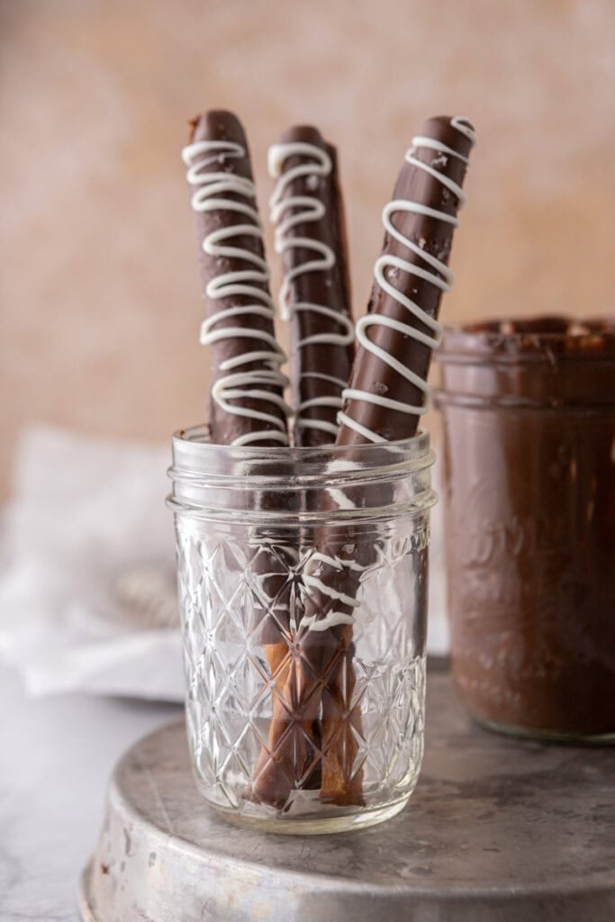 three caramel chocolate covered pretzel rods in a cup