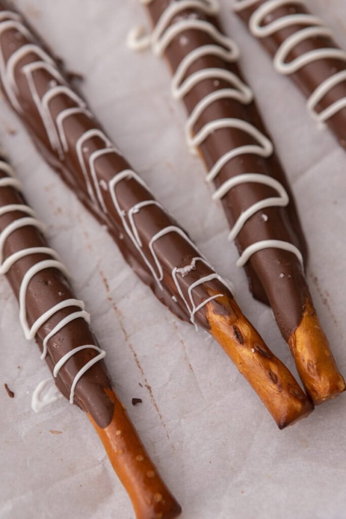 close up of three caramel chocolate covered pretzel rods on a sheet pan