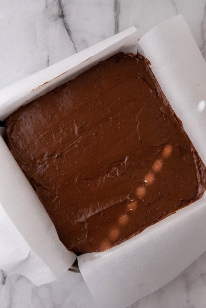 Chocolate candy filling spread evenly in a parchment-lined square baking dish before freezing.
