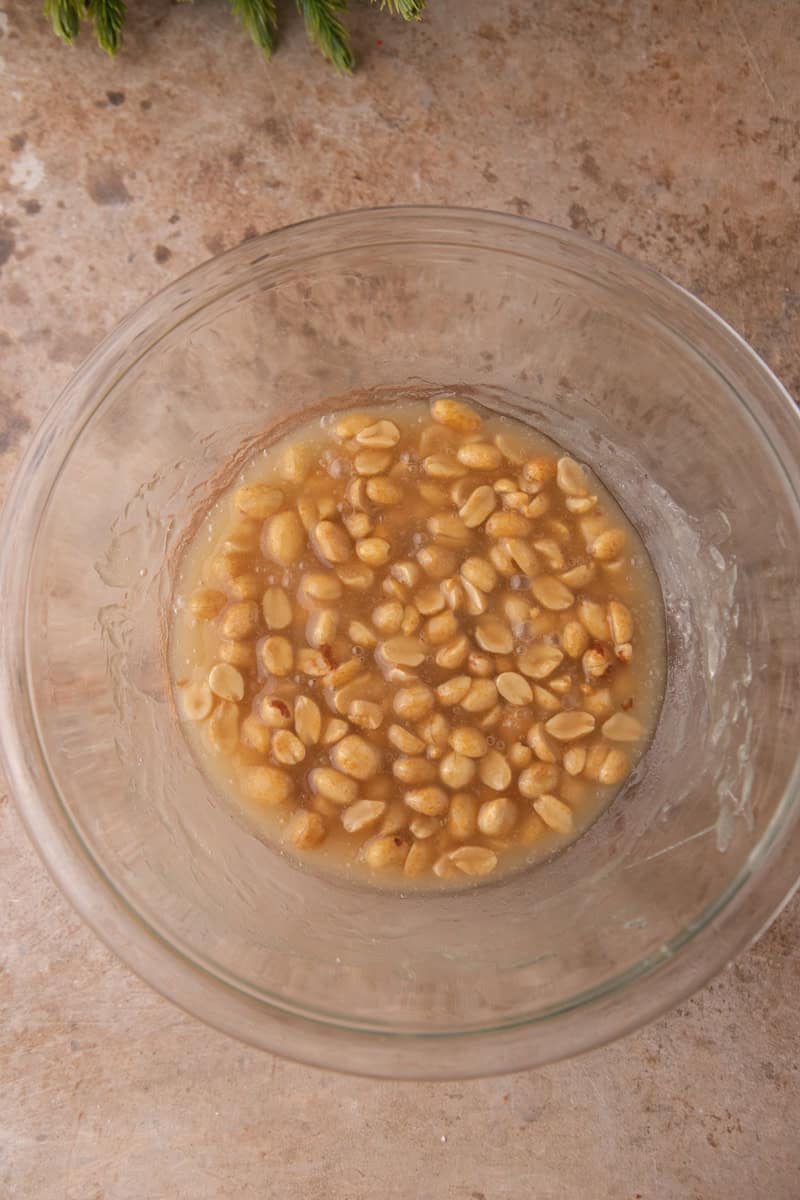 Peanuts and butter stirred into the hot sugar syrup in a glass bowl.