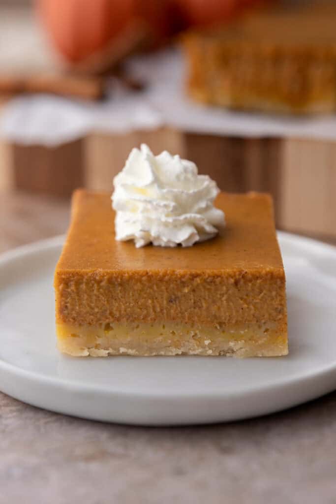 Pumpkin pie bar on a white plate showing the creamy filling over a golden shortbread crust.