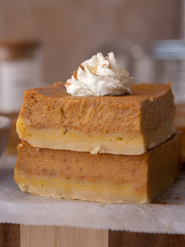 Creamy pumpkin pie bars with shortbread crust sliced into squares and topped with whipped cream.