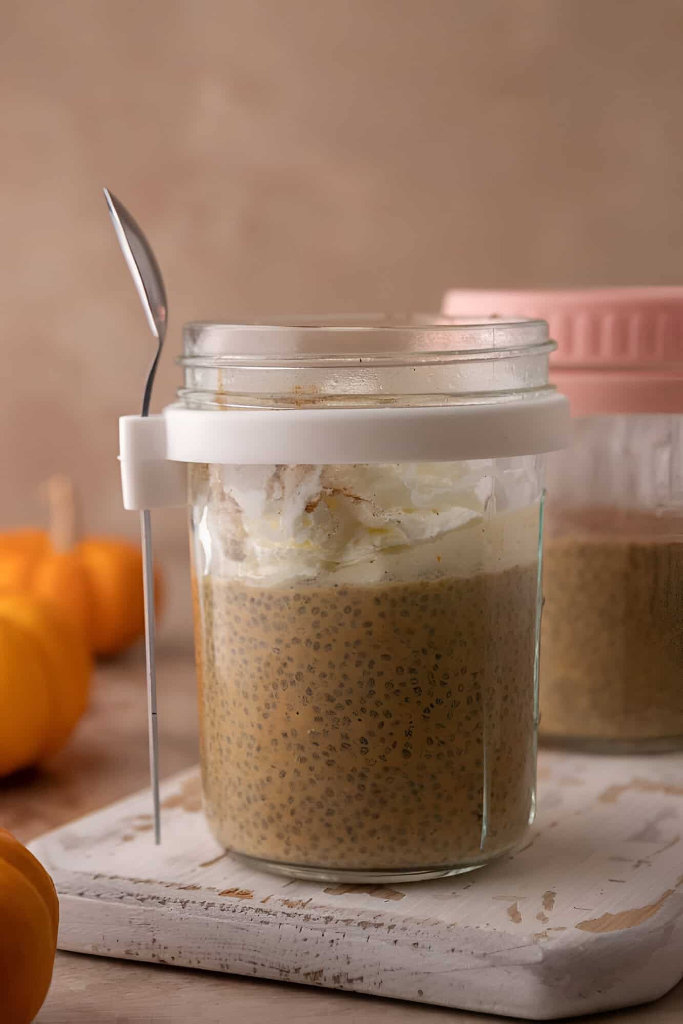 Pumpkin chia seed pudding in a glass jar topped with whipped cream, with mini pumpkins nearby.
