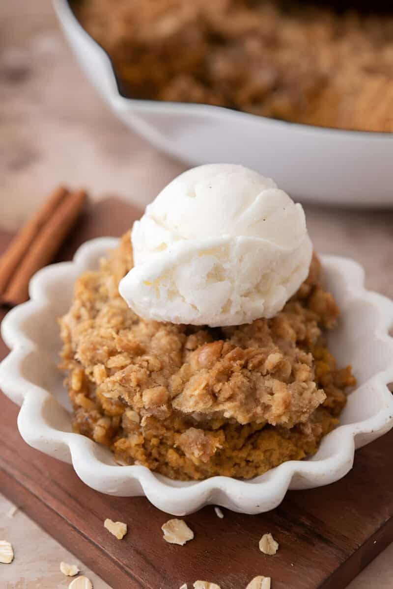 Pumpkin crisp with a crunchy oat crumble topping and vanilla ice cream in a scalloped bowl.