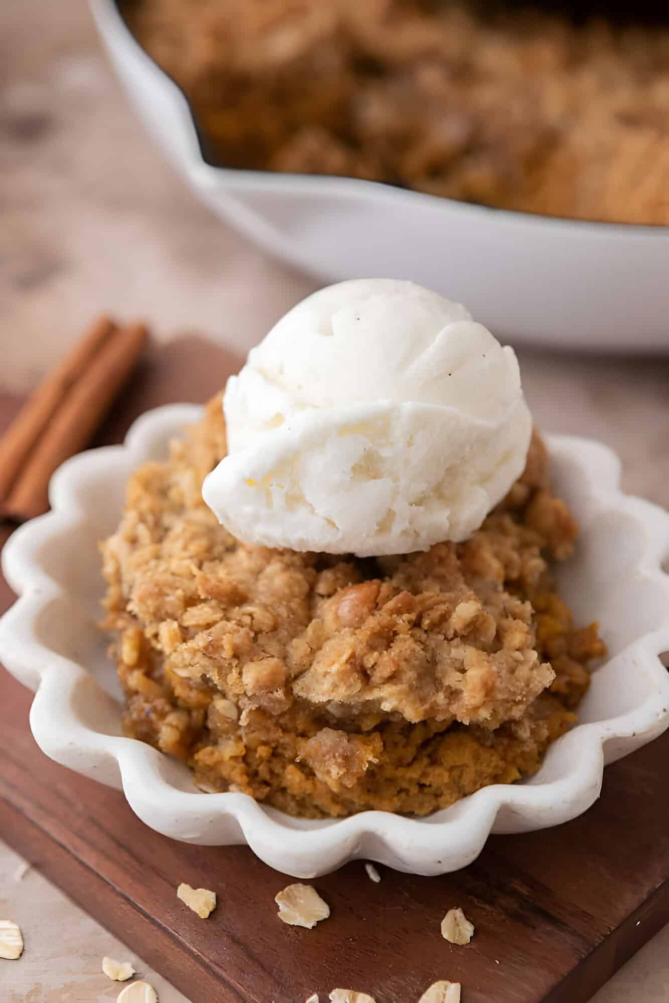 Warm serving of pumpkin crisp topped with vanilla ice cream on a board with cinnamon sticks.