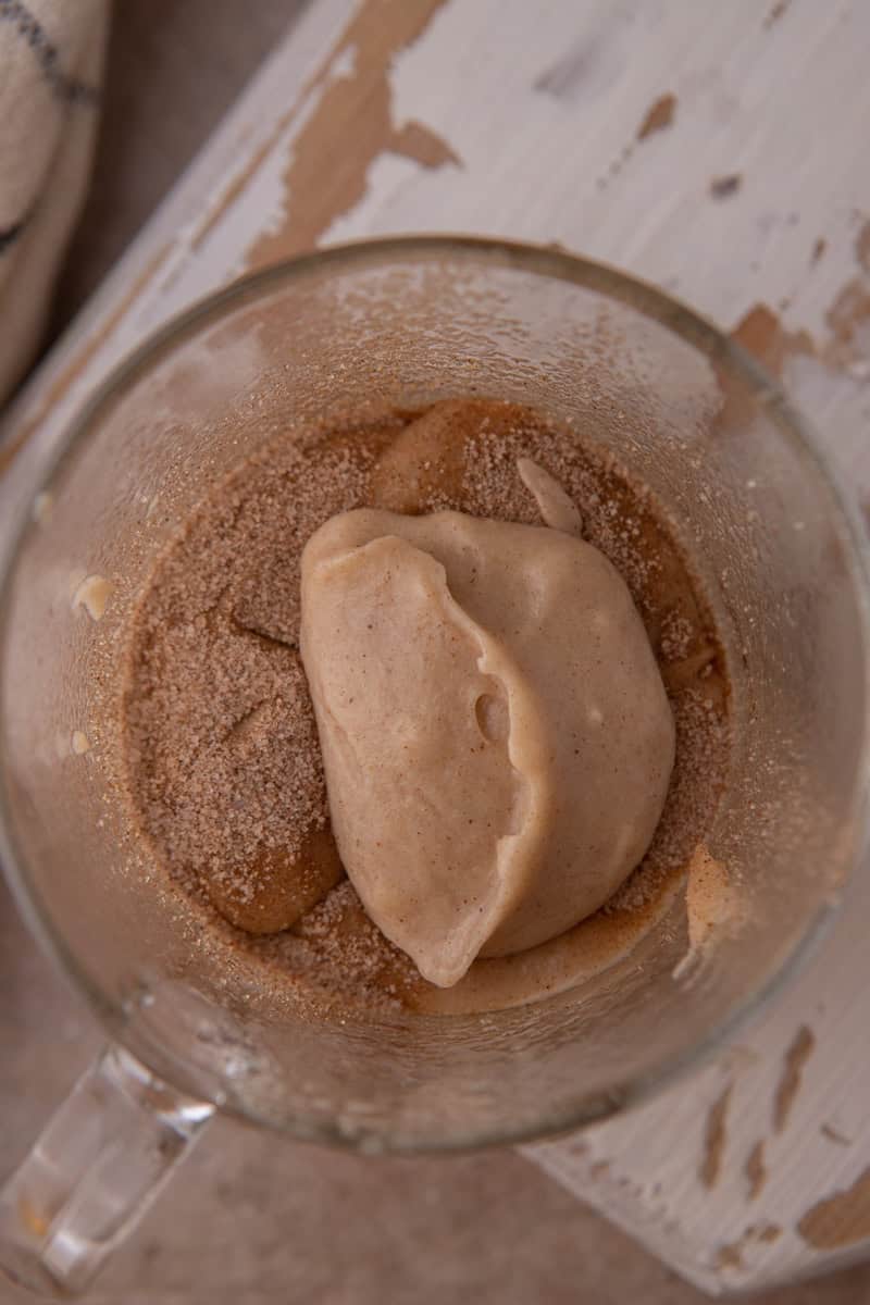 A spoonful of snickerdoodle batter on a layer of cinnamon sugar inside a glass mug, seen from above.