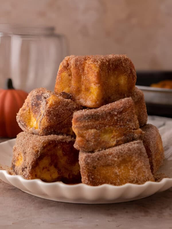 Golden Hawaiian roll pumpkin French toast bites coated in cinnamon sugar and stacked on a white plate.