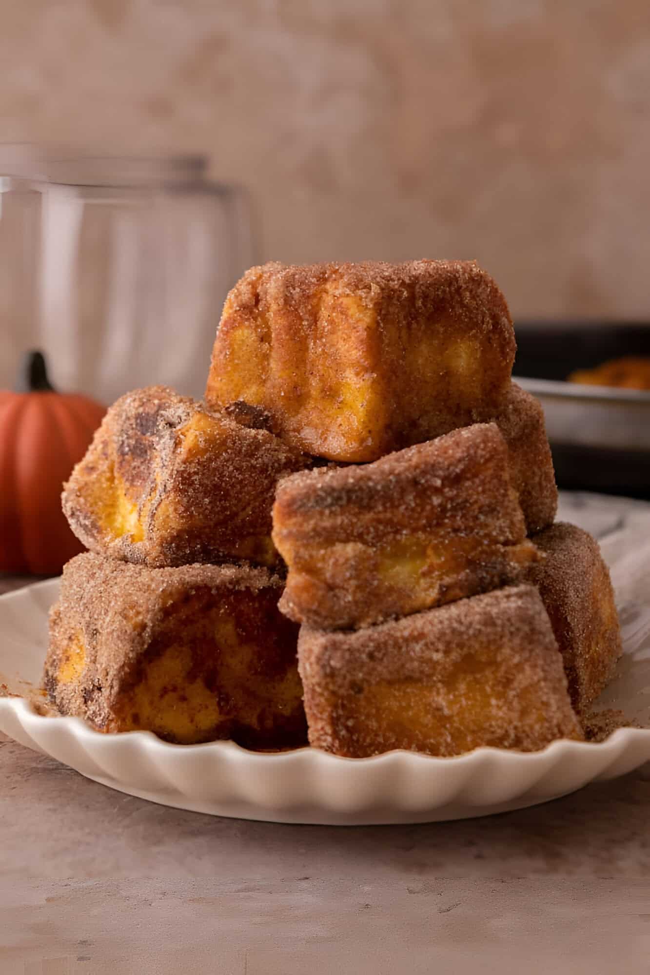 Golden Hawaiian roll pumpkin French toast bites coated in cinnamon sugar and stacked on a white plate.